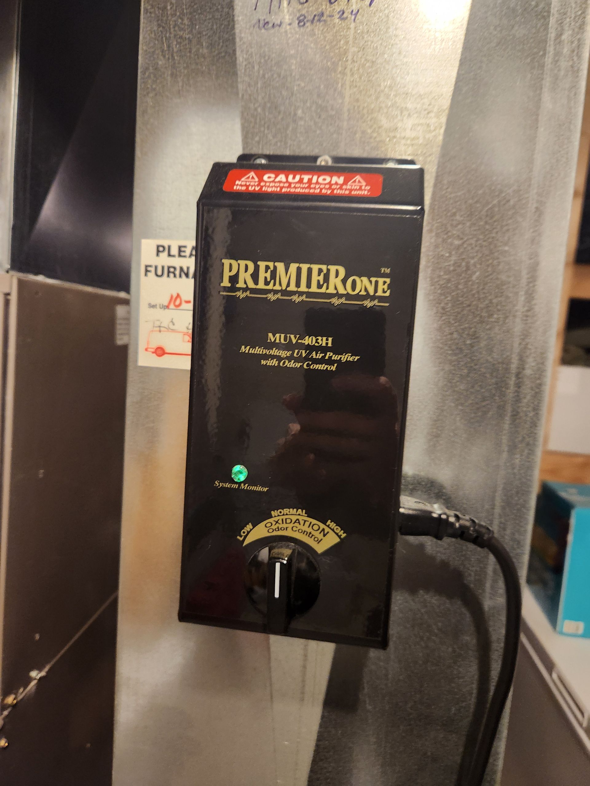 Black Premier One air cleaner attached to a metallic duct, with a power cord and a green light illuminated.