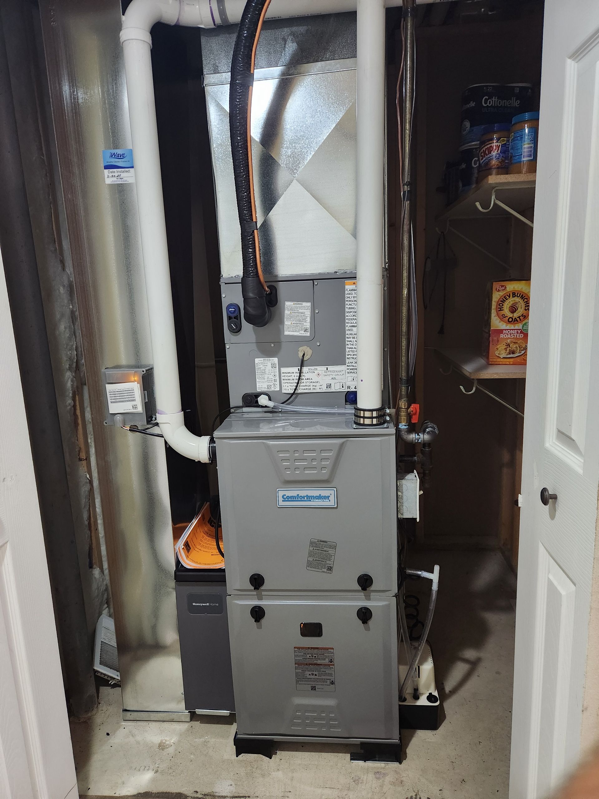 A central heating unit with silver metal components installed in a utility closet with a white door.
