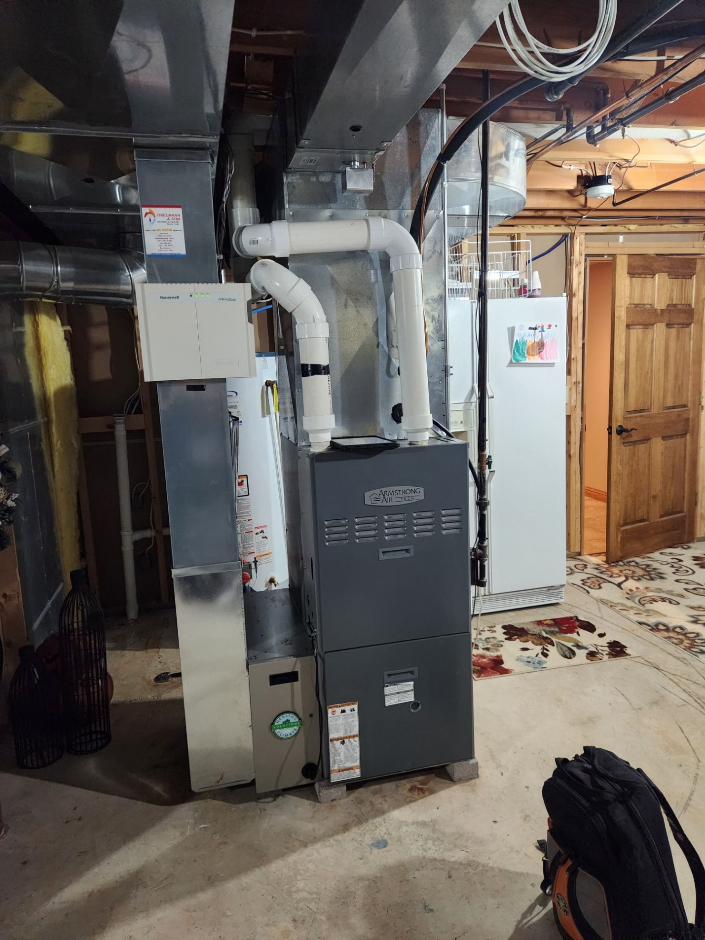 A furnace and ductwork in a basement. Grey unit with white pipes and an attached water heater.