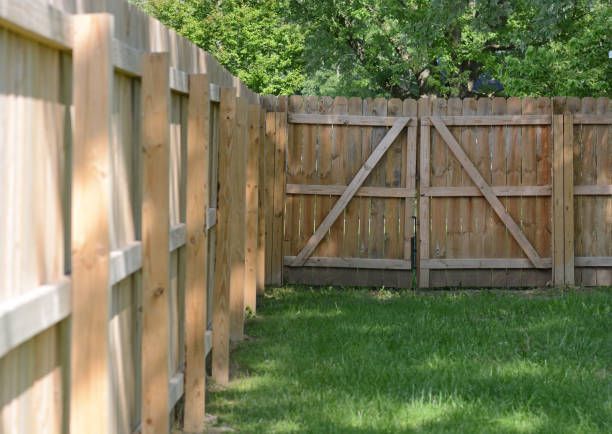 Wooden privacy fencing with a double gate enclosing a green backyard surrounded by trees.