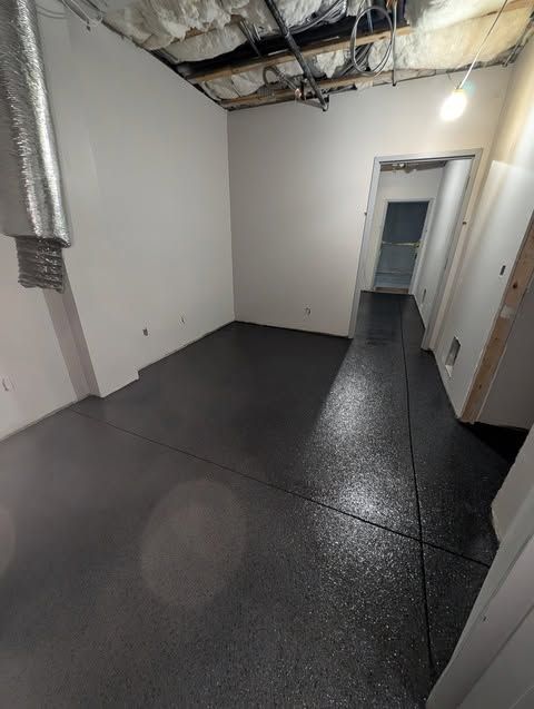 Empty unfinished basement room with exposed ceiling, gray walls, and dark floor leading to a doorway