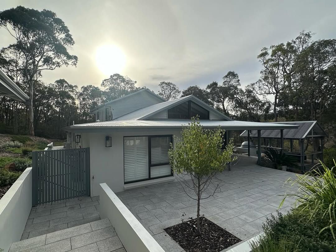 Modern house with gray roof, paved courtyard, and trees at sunset