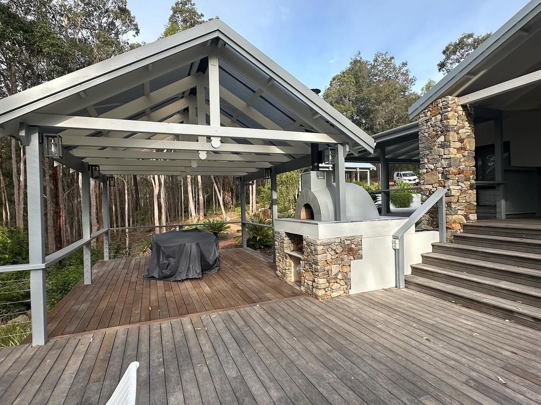 Outdoor patio with wooden deck, stone fireplace, and covered seating area beside stairs and trees