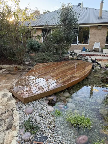 Backyard pond with a wooden footbridge, rocks, and a house in the background