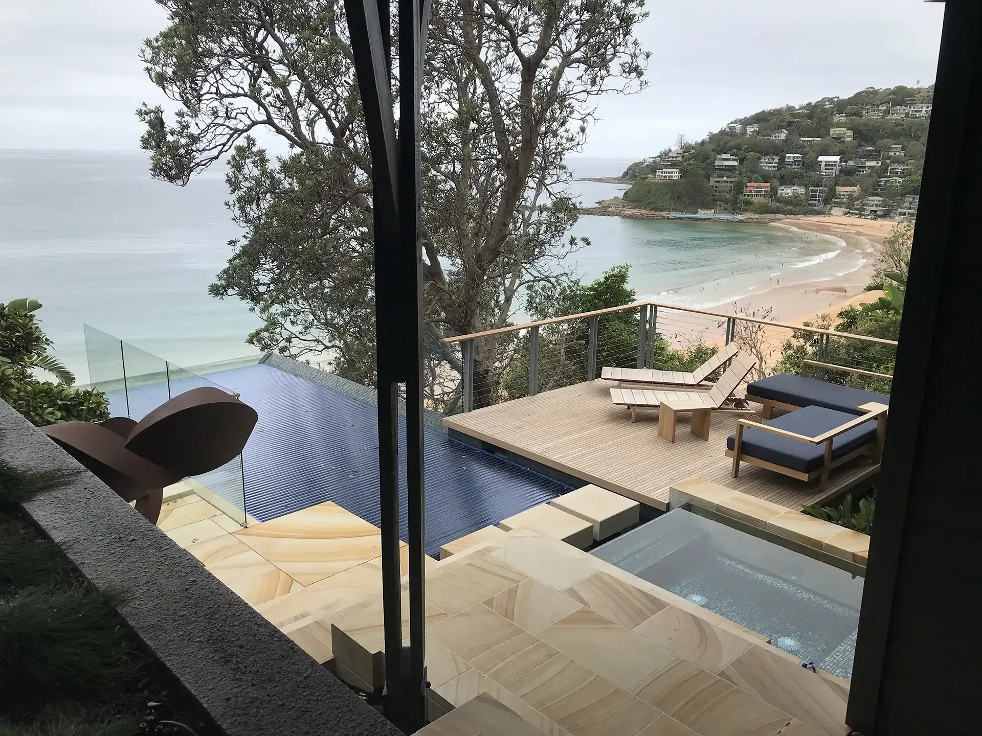Modern seaside terrace with infinity pool, lounge chairs, and a view of a beach and bay