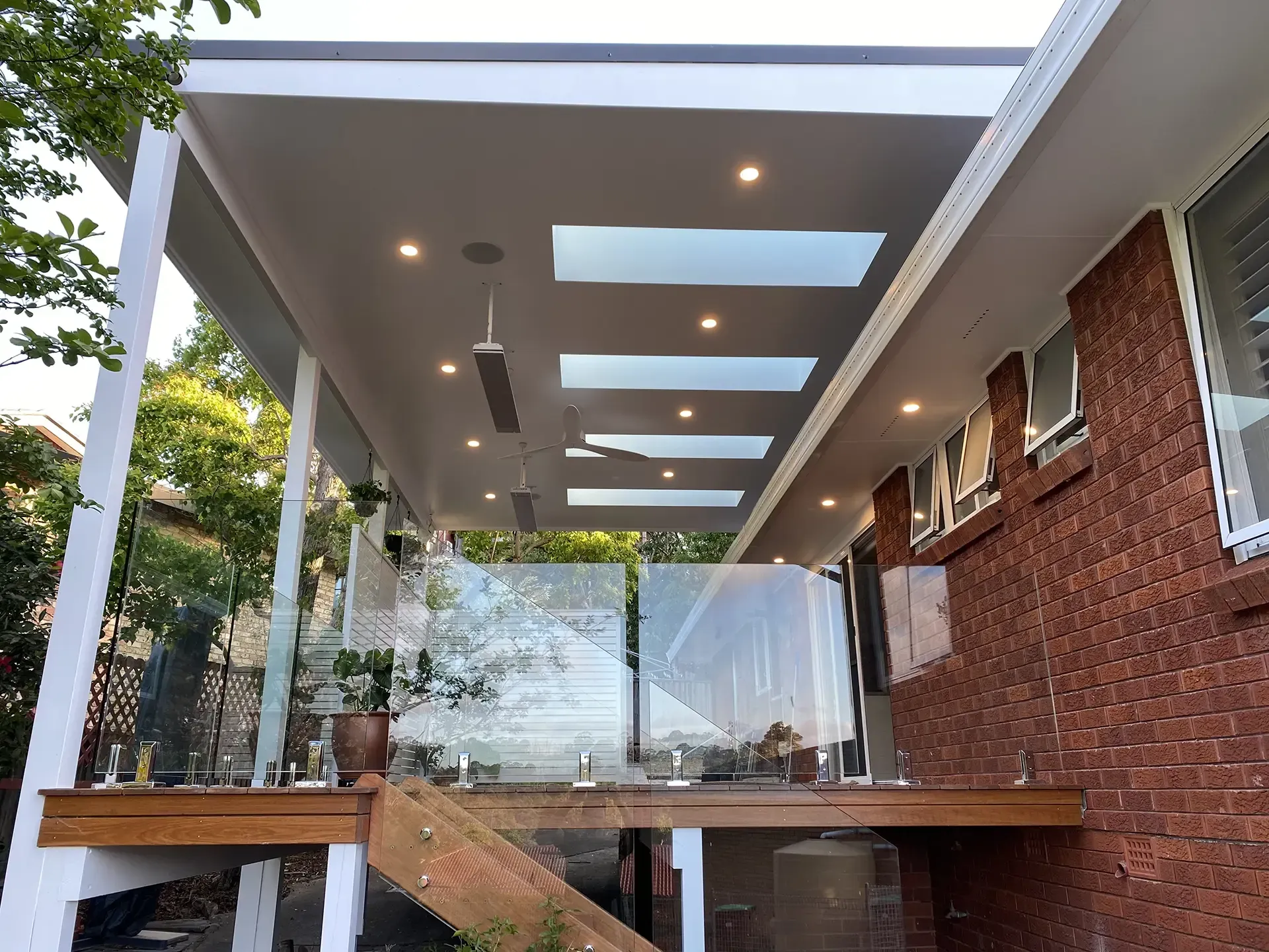 Modern house exterior with a covered patio, glass railing, skylights, and brick walls