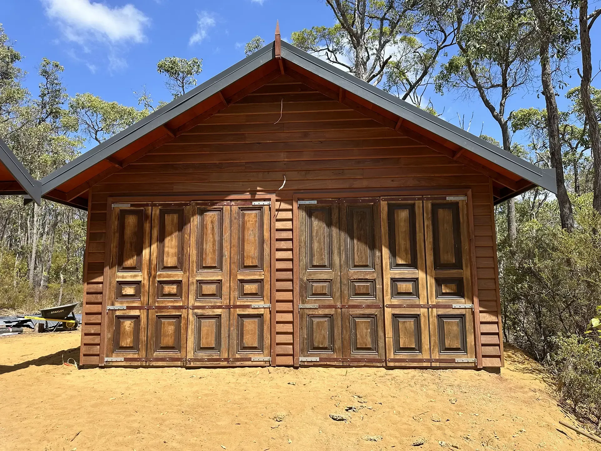 Wooden cabin with paneled double doors in a sunny wooded area