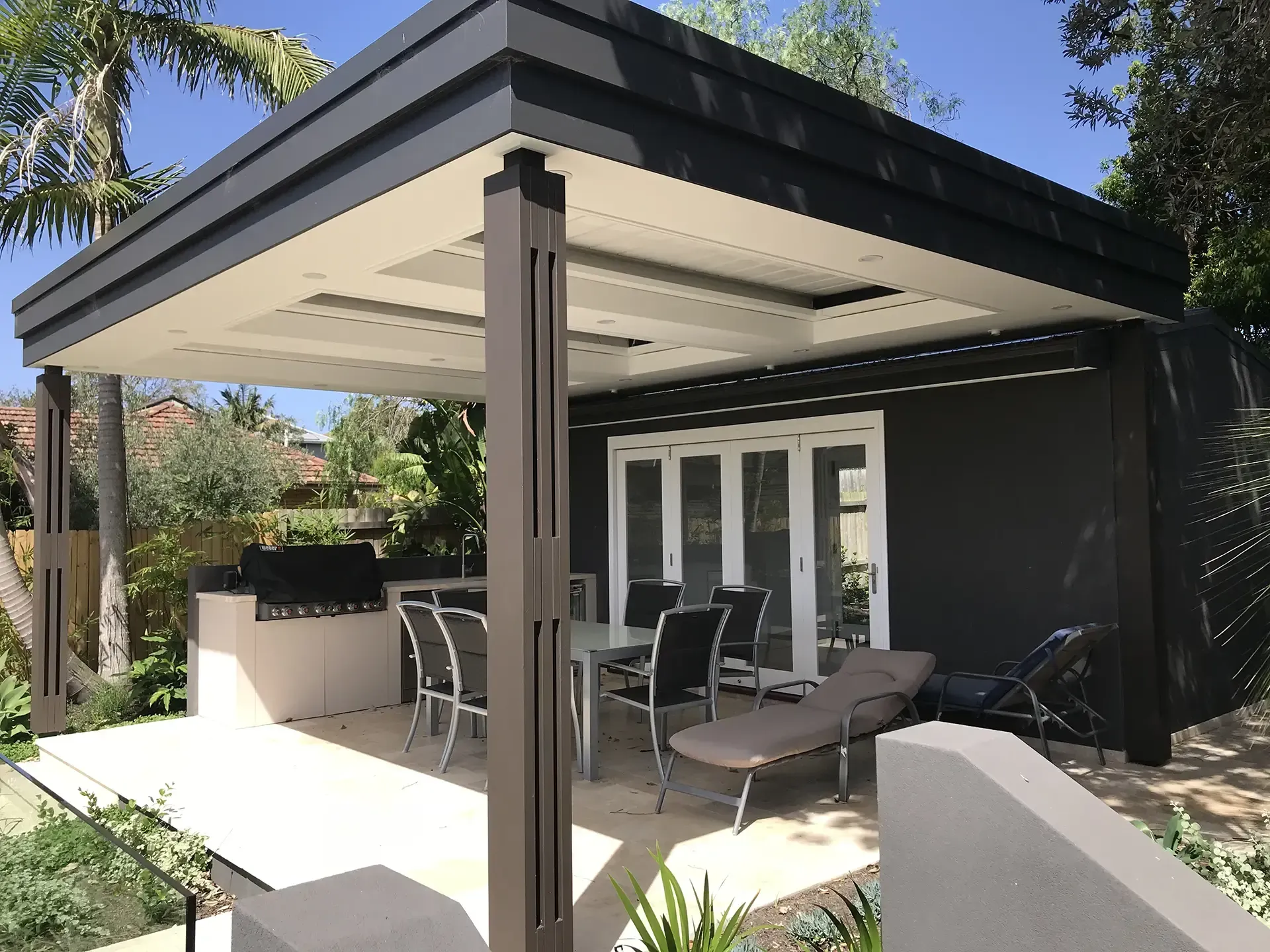 Modern patio with covered pergola, outdoor dining table, lounge chairs, and white double doors