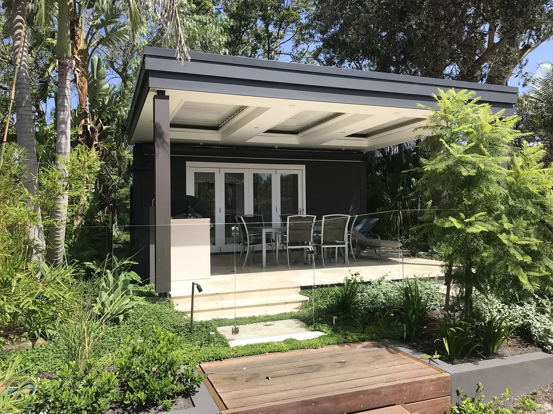 Modern patio with outdoor dining set under a covered pergola, surrounded by lush greenery.