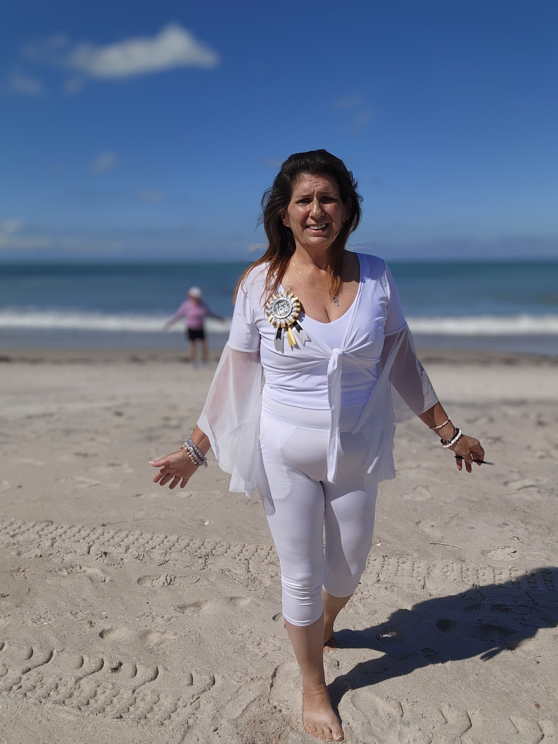 A woman in a white dress is walking on the beach.