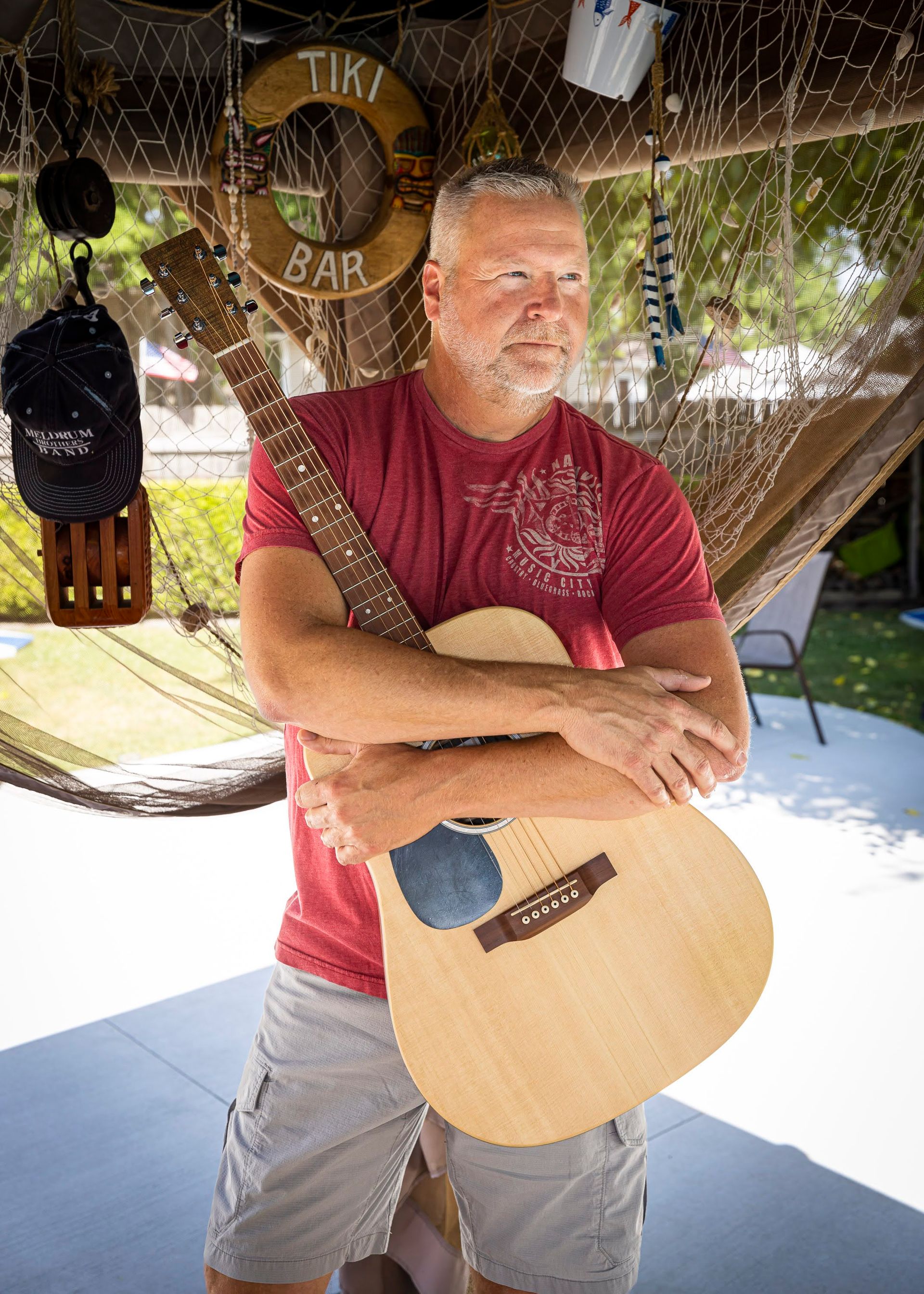 Chris Meldrum in a red shirt is holding a guitar.