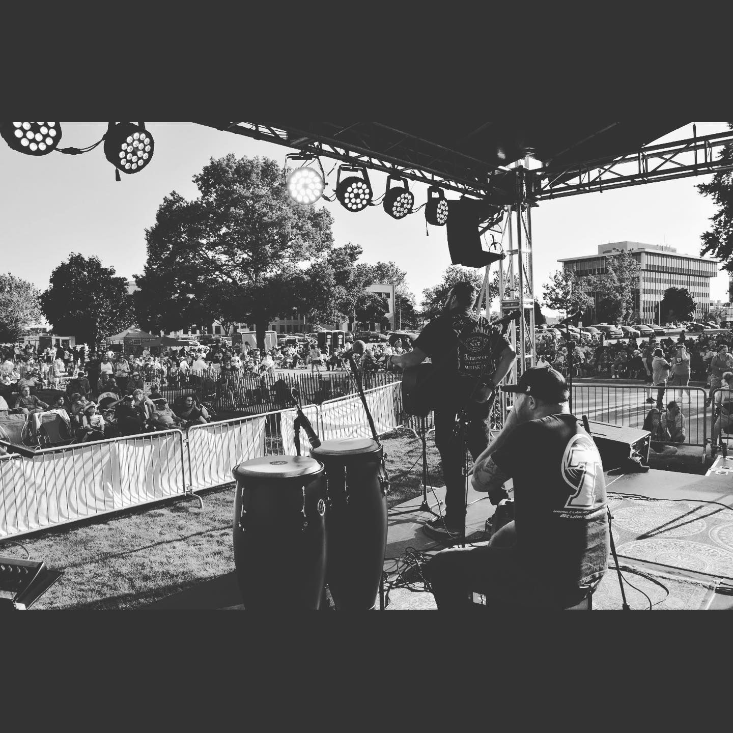 Man playing acoustic guitar, wearing a cap and black jacket, recording in a studio near a window.