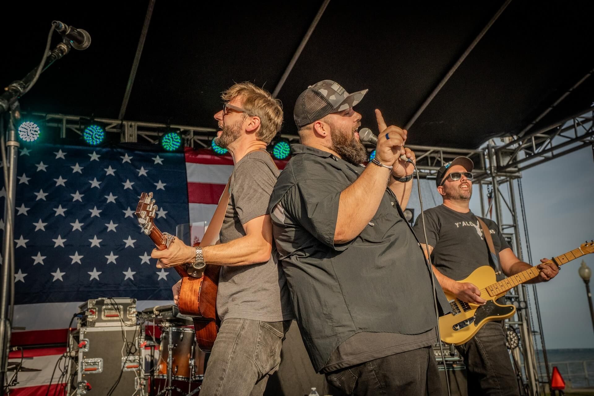 Live band performing onstage in front of a large American flag backdrop.