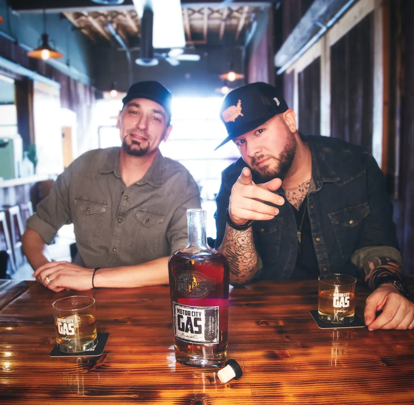 Two men are sitting at a table with a bottle on it.
