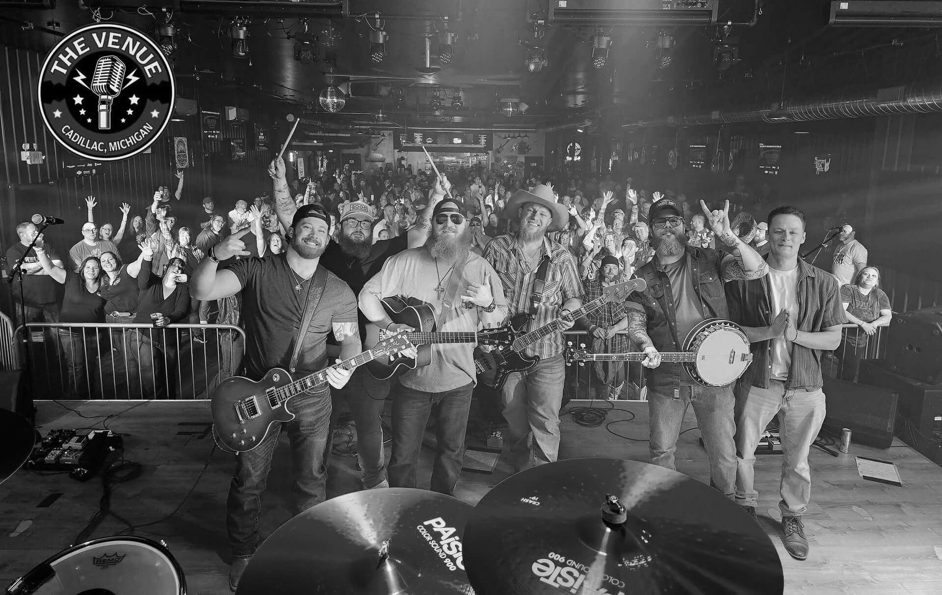 Band performing on stage before a cheering crowd, with drums visible in the foreground.