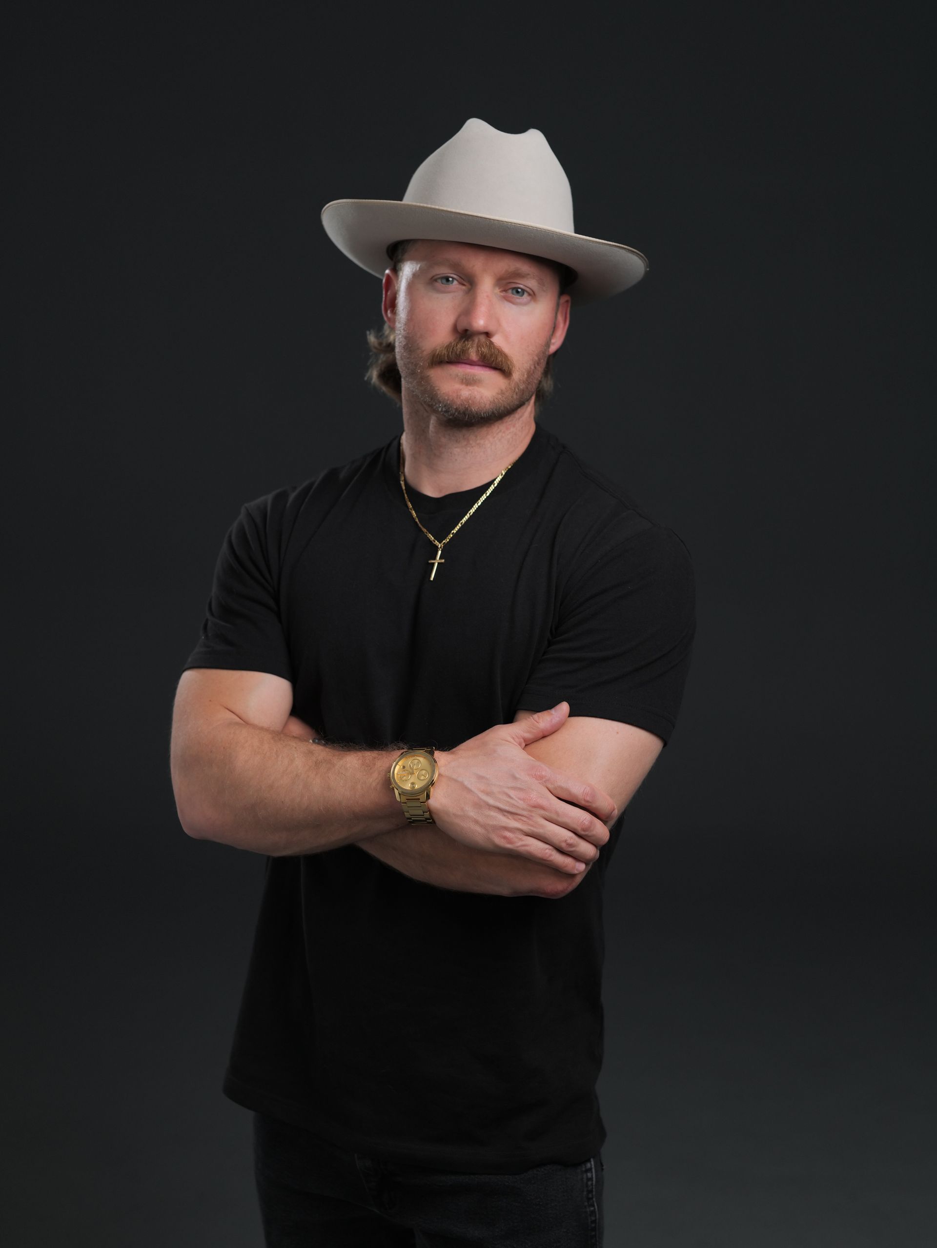 Rob Stone in a white cowboy hat and black shirt posing with arms crossed against a dark background.