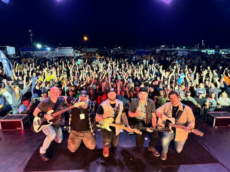 A group of men playing guitars on a stage in front of a crowd.