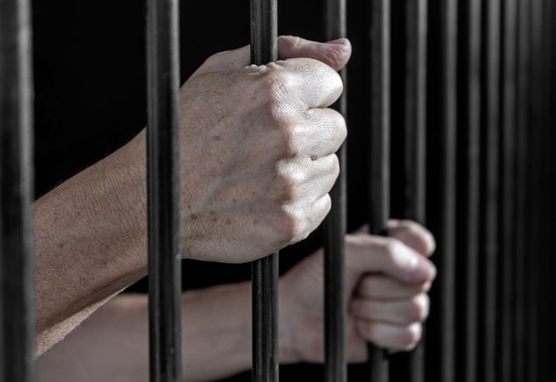 Hands gripping prison bars in a dark jail cell