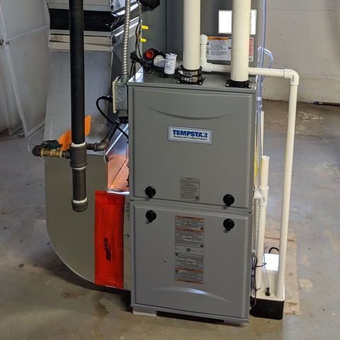 A gray Tempstar HVAC furnace unit standing in a basement with attached white PVC venting pipes and a gas line.