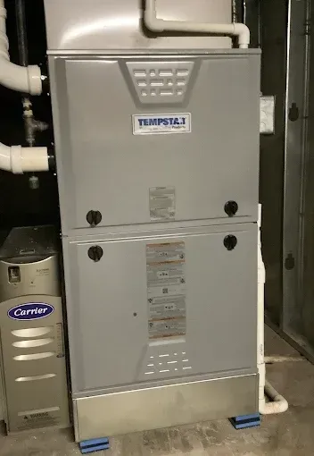 A Tempstar high-efficiency gas furnace and a Carrier unit sit on a basement floor with PVC piping connected.