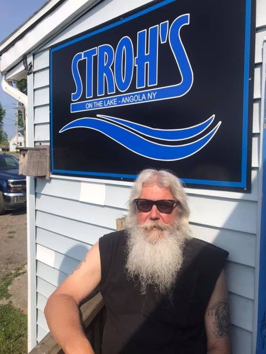 A man with a beard is standing in front of a stroh 's sign