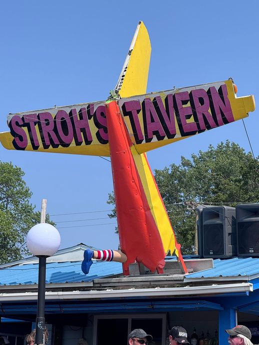 A sign for stroh 's tavern is shaped like an airplane