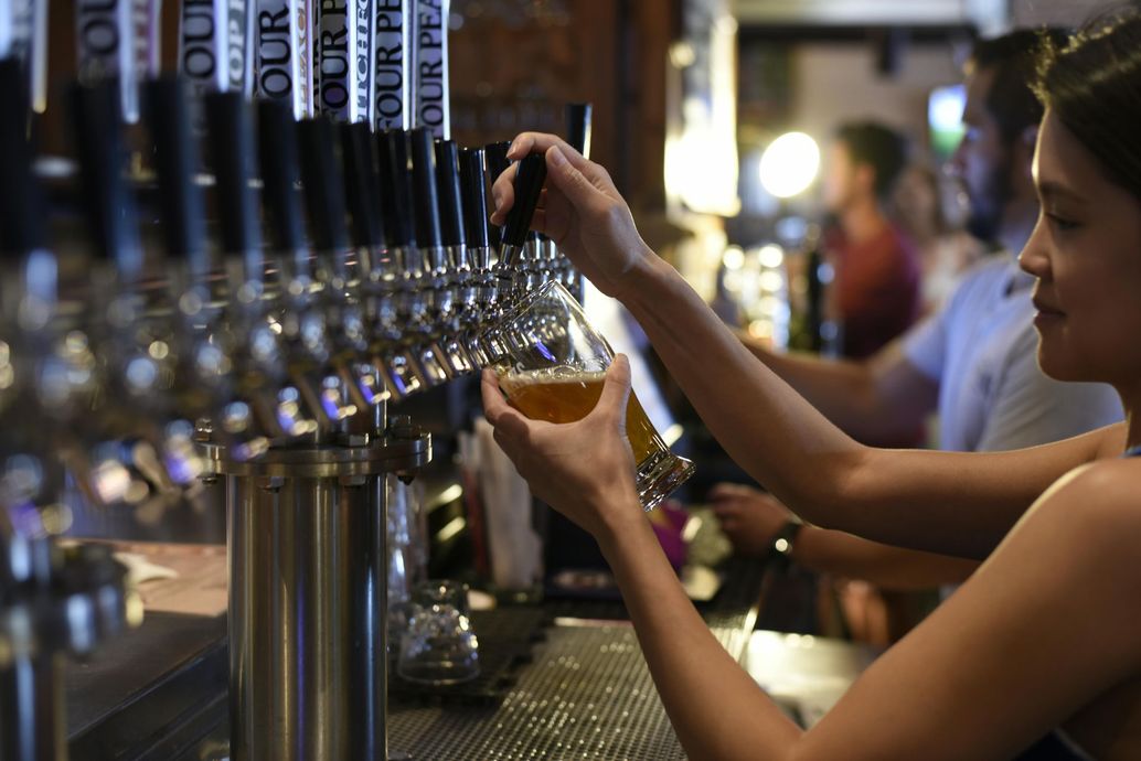 A woman is pouring beer into a glass at a bar.
