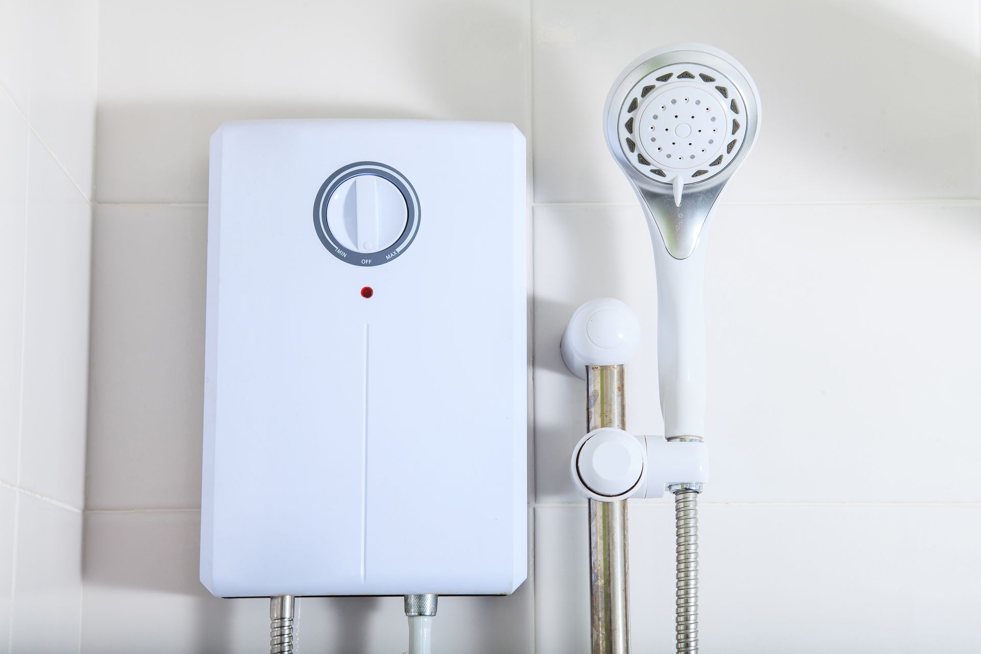 White electric shower unit mounted on white tiled wall next to shower head and rail.