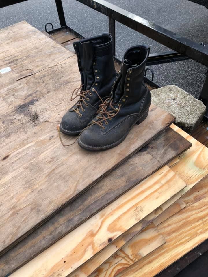 A pair of black boots are sitting on top of a pile of wood.