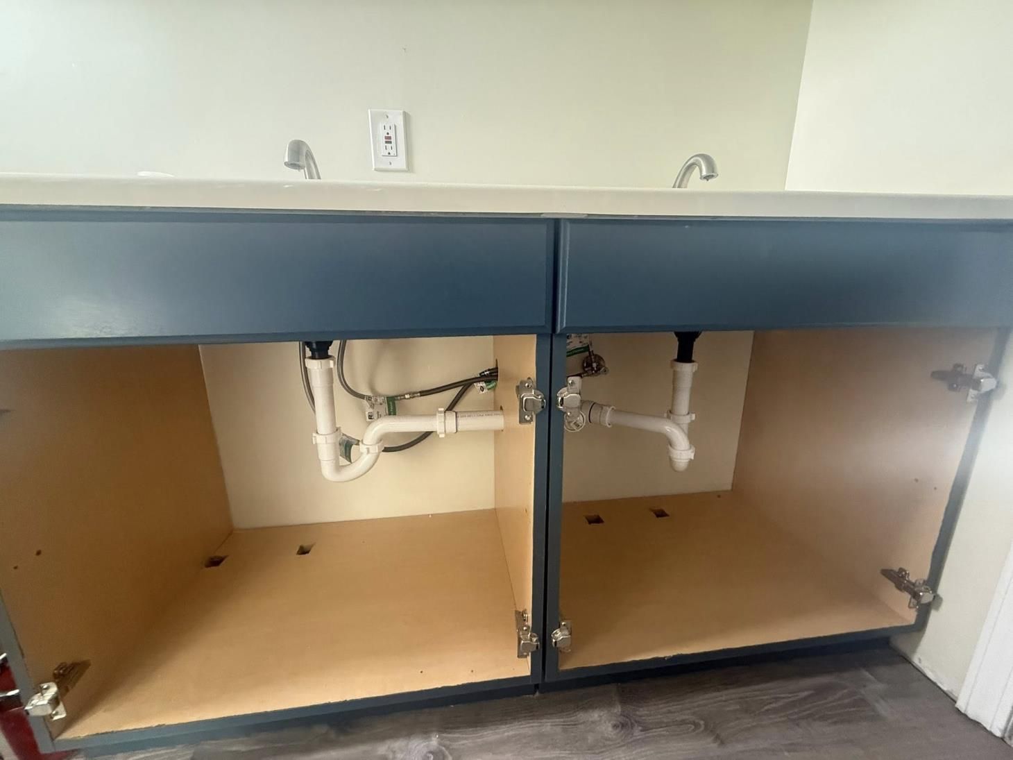 Double sink vanity with blue cabinets, beige interior, and exposed plumbing.