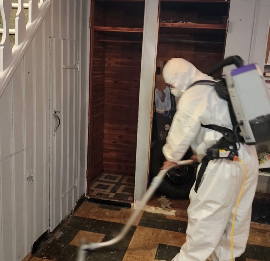 Person in protective suit vacuuming a room, possibly for mold removal.