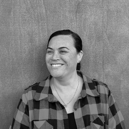 Woman smiling, wearing earrings and necklace, against a textured wall.