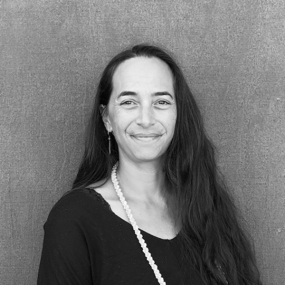 Woman with long dark hair smiles, wearing a black top and pearl necklace, in front of a textured background.