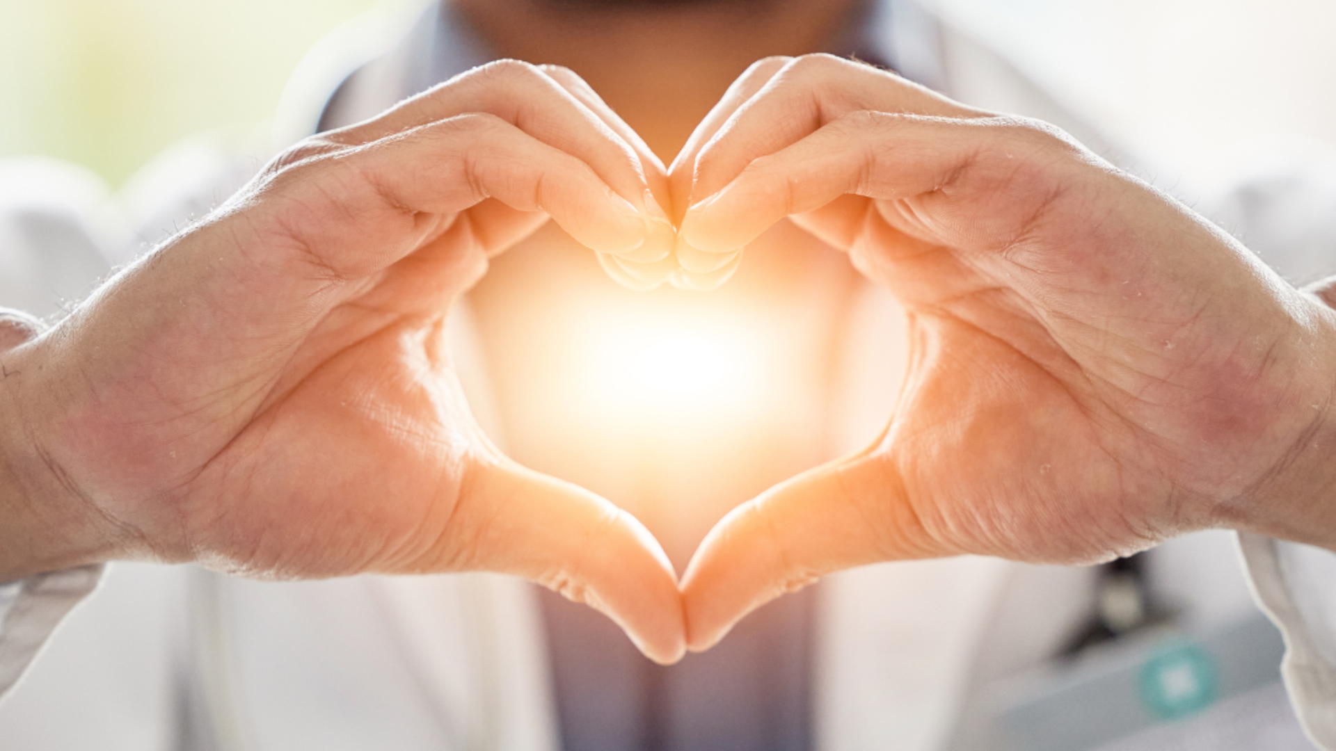 Doctor's hands forming heart shape around bright light; healthcare symbol.