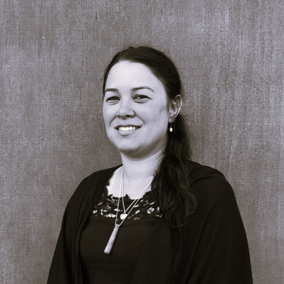 Smiling woman in a dark top with a pendant, standing in front of a wood-grain wall.