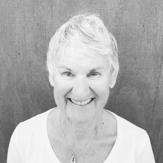 Woman with brown hair smiles broadly, wearing a black top and silver necklace, against a textured wall.