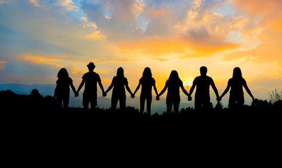 Silhouetted people holding hands against a colorful sunset, symbolizing unity and friendship outdoors.