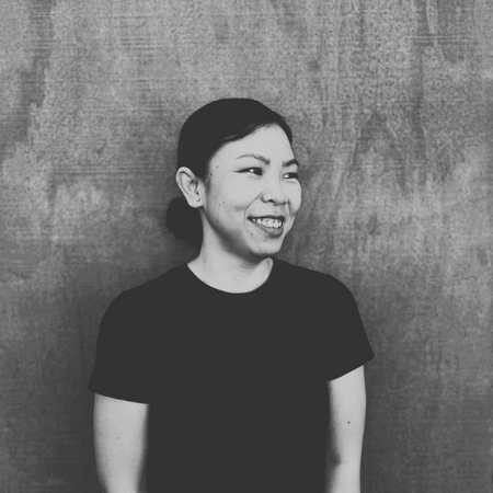 Woman with dark hair smiling, wearing a dark t-shirt, against a wooden background.