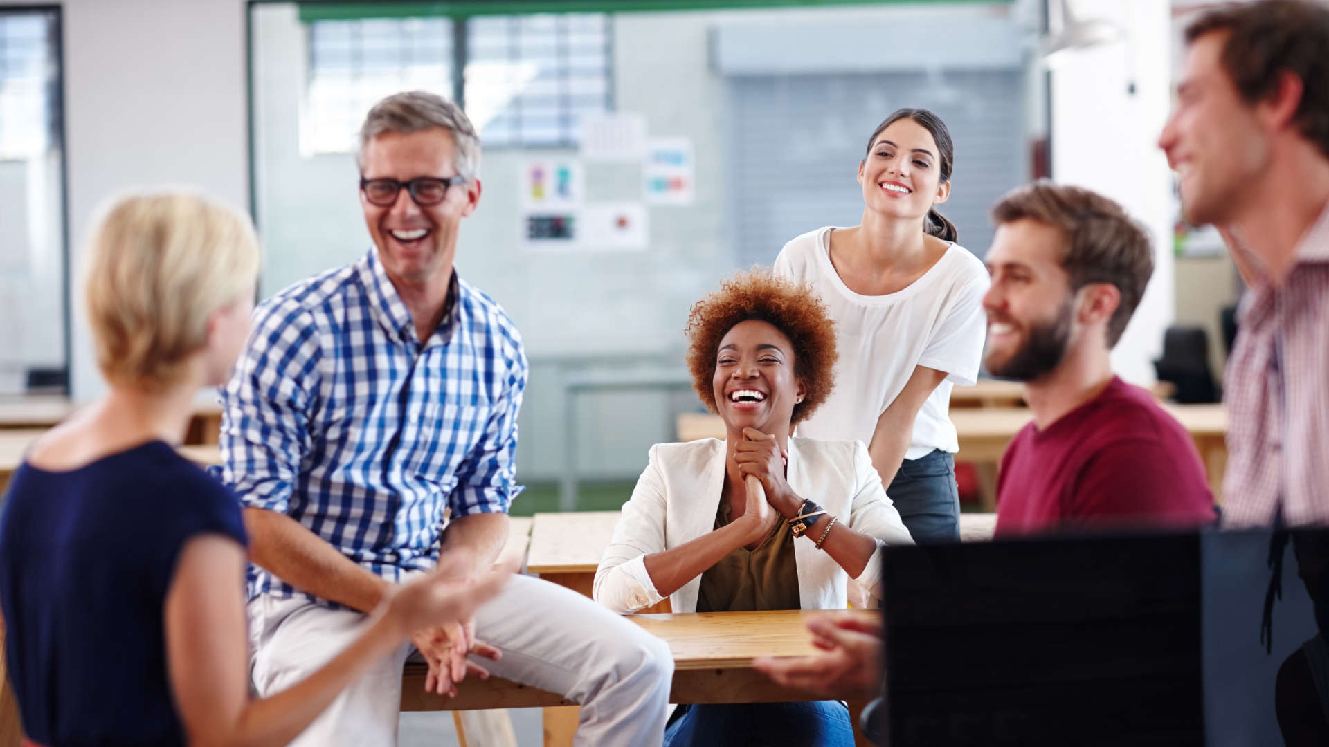 Group of coworkers laughing and talking in a modern office setting.