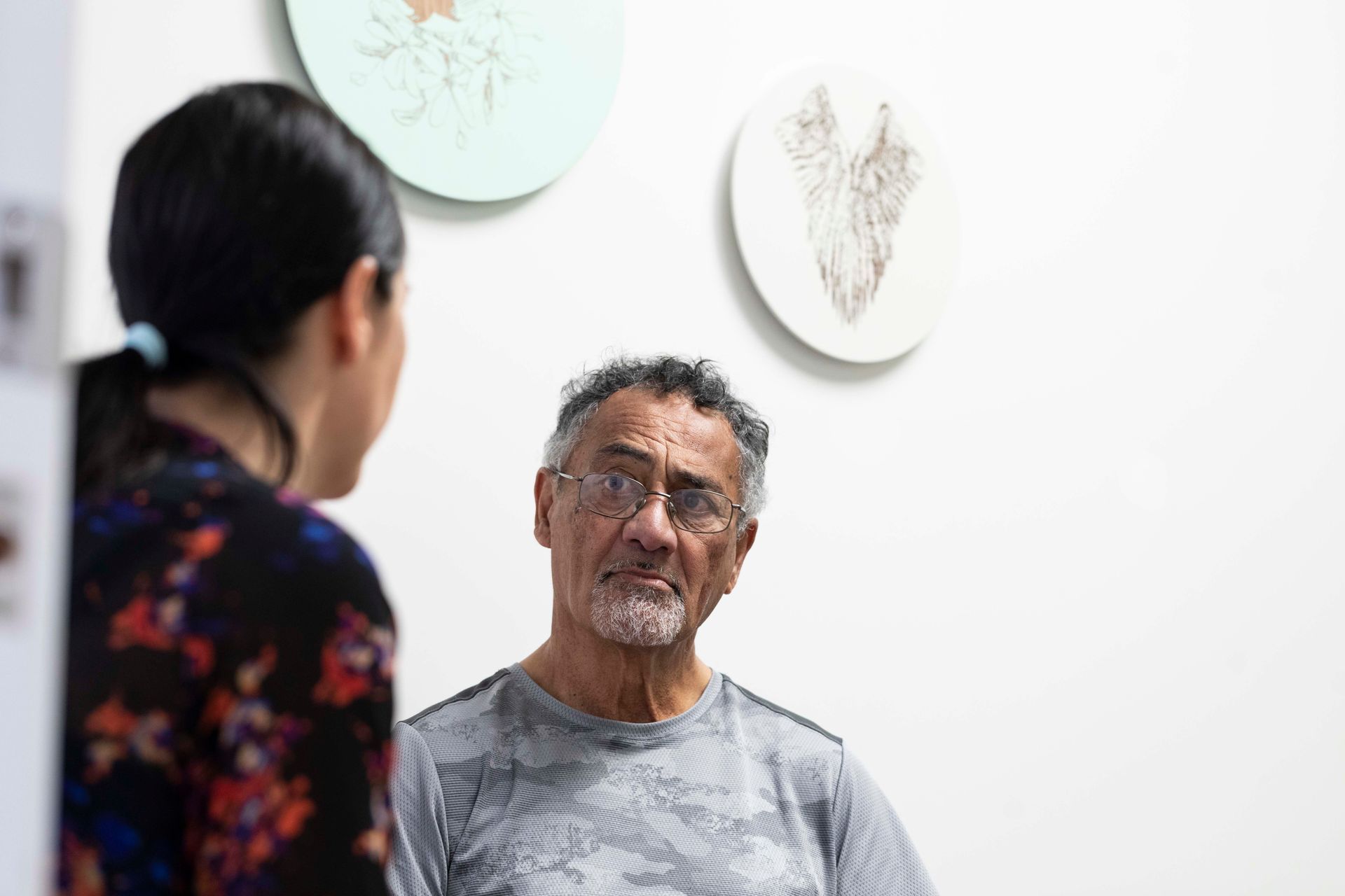 Man in glasses listening to person, art on wall.