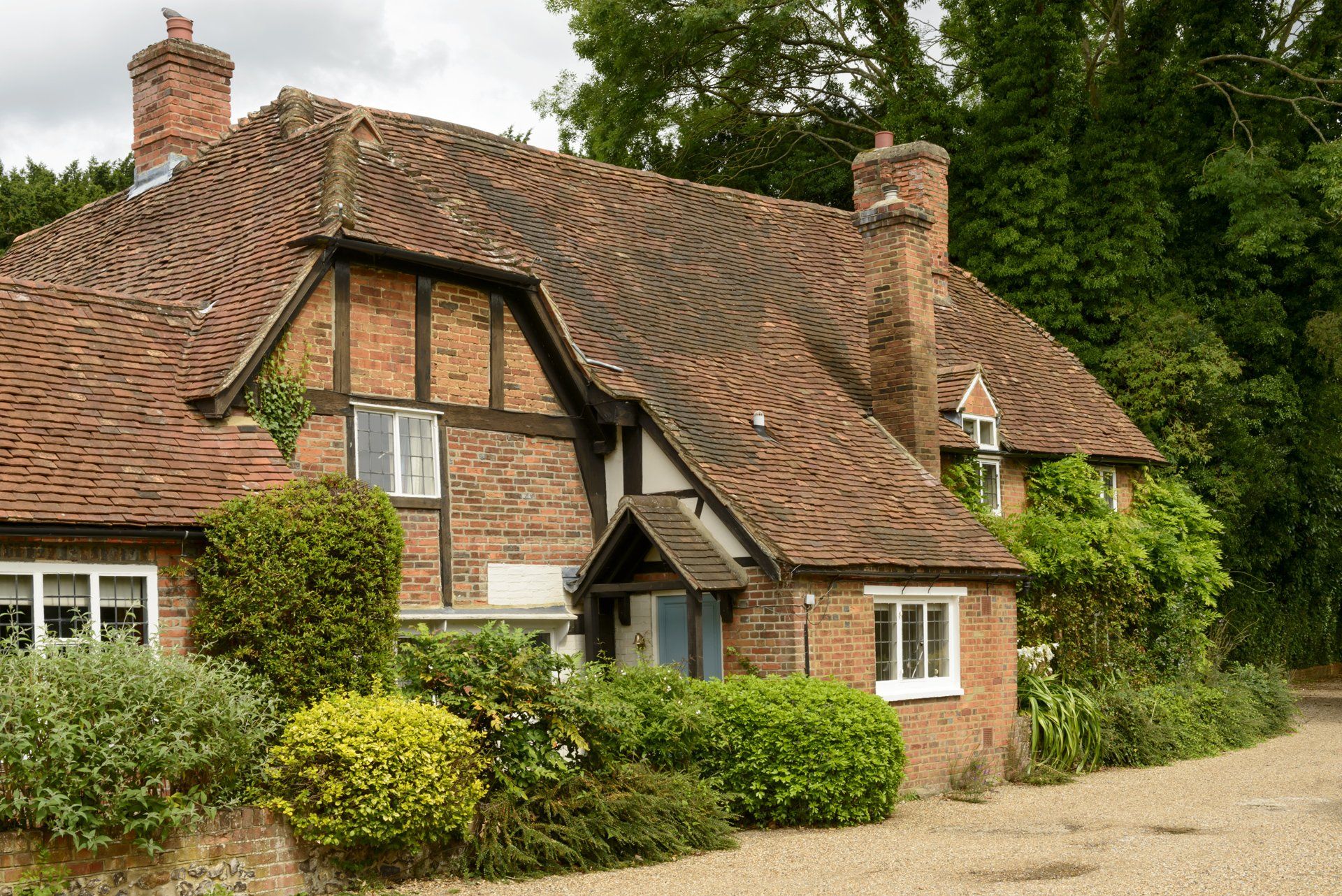A brick house with a tiled roof is surrounded by trees and bushes.