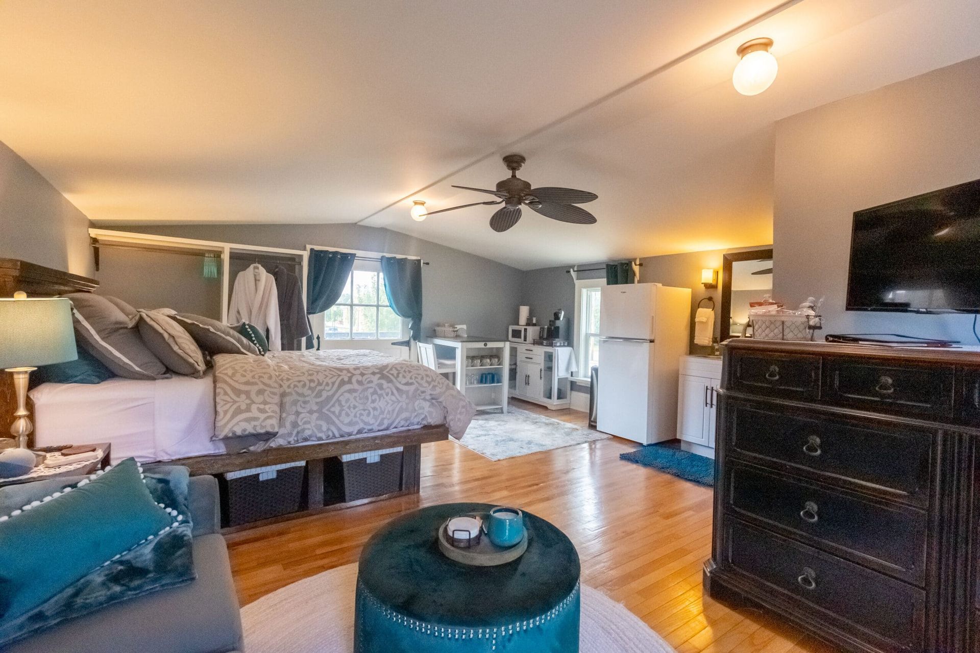 A bedroom with a bed , dresser , ottoman and television.