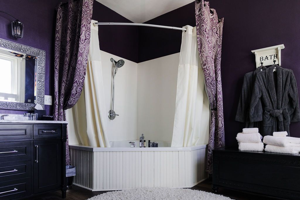 Purple bathroom with corner shower, black vanity, and bathrobe.