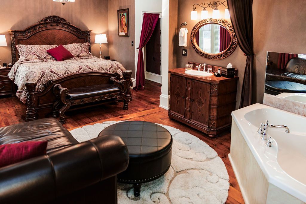 Luxurious bedroom with a large bed, vanity, and jacuzzi tub. Dark wood furniture and red accents.