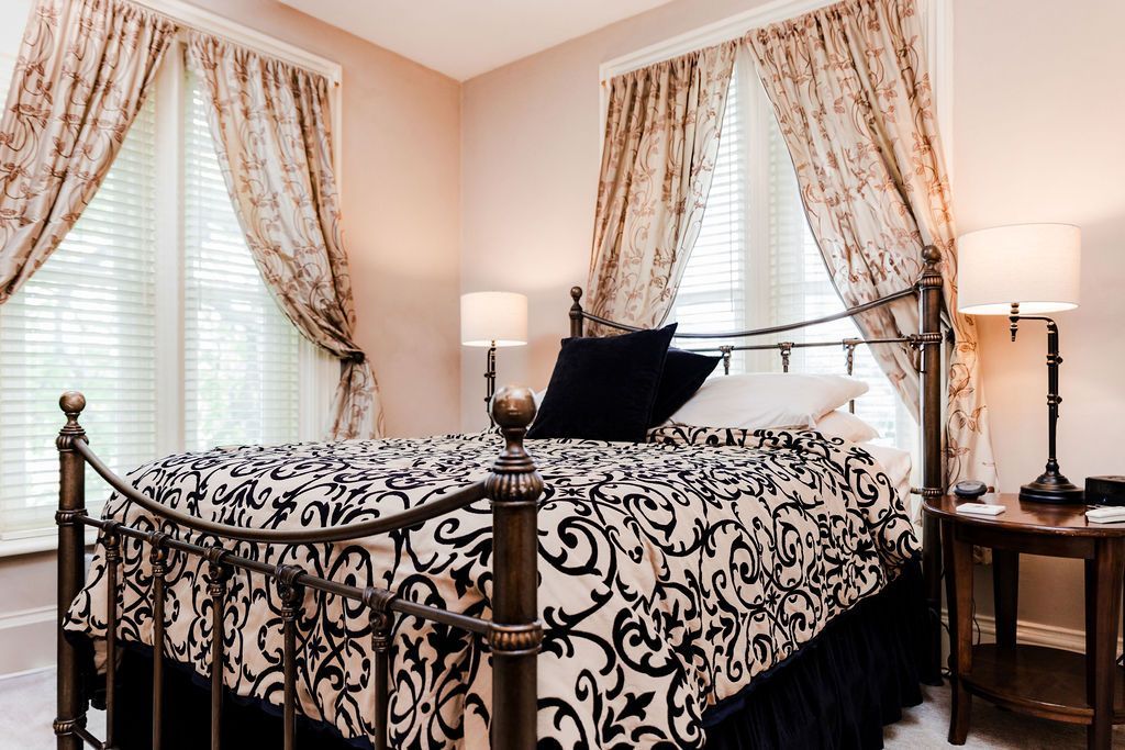 Bedroom with a wrought iron bed, black and white bedding, and floral curtains.