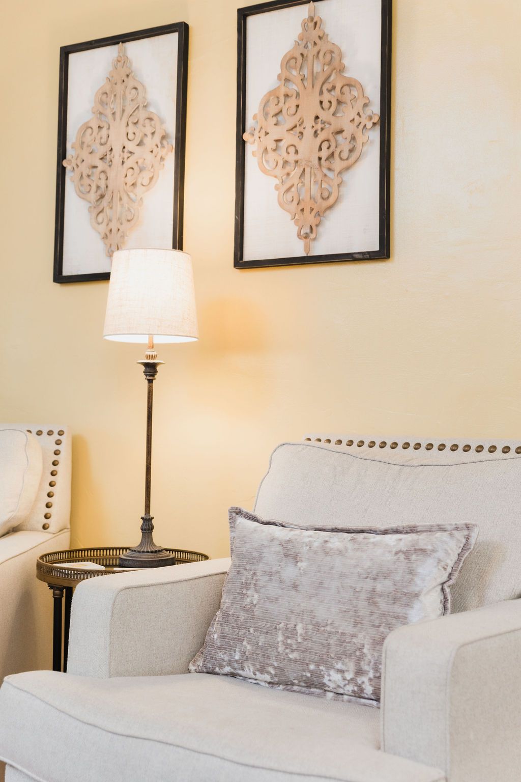 Beige armchair with sequin pillow, floor lamp, decorative wall art against yellow wall.