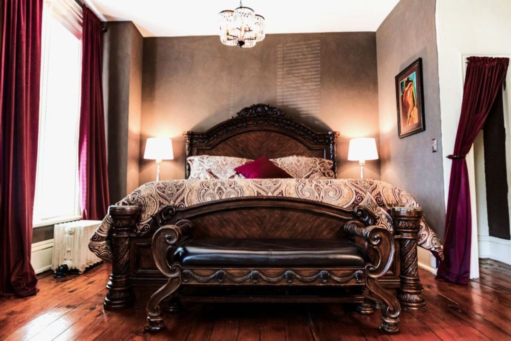 Luxurious bedroom with large dark wood bed, burgundy drapes, and a crystal chandelier.