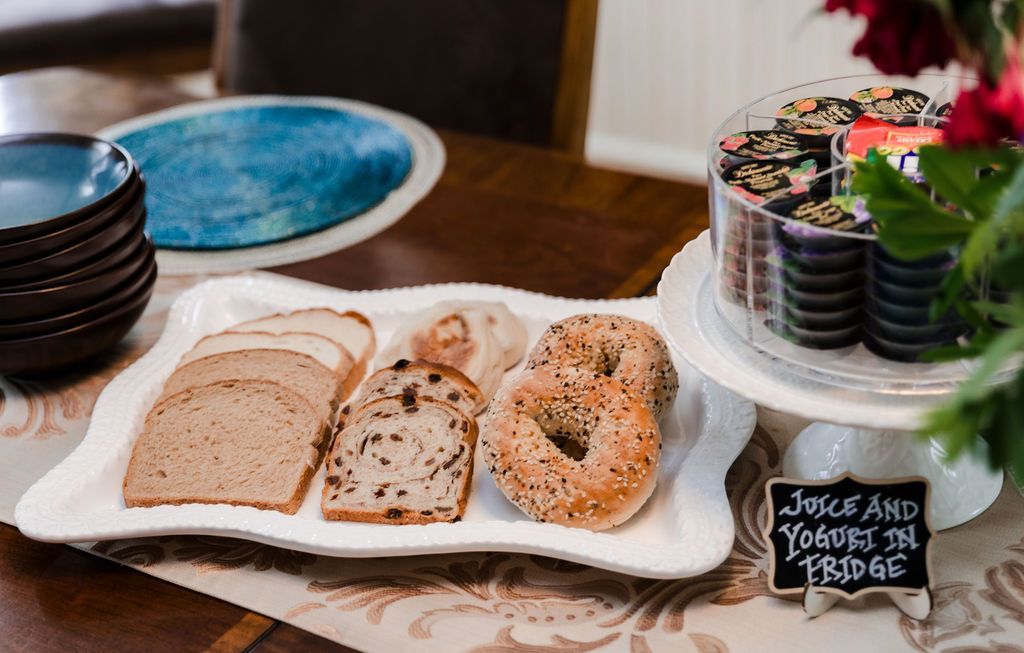 Breakfast spread: sliced bread, bagels, pastries on a white tray, alongside other dishes and a cake stand.