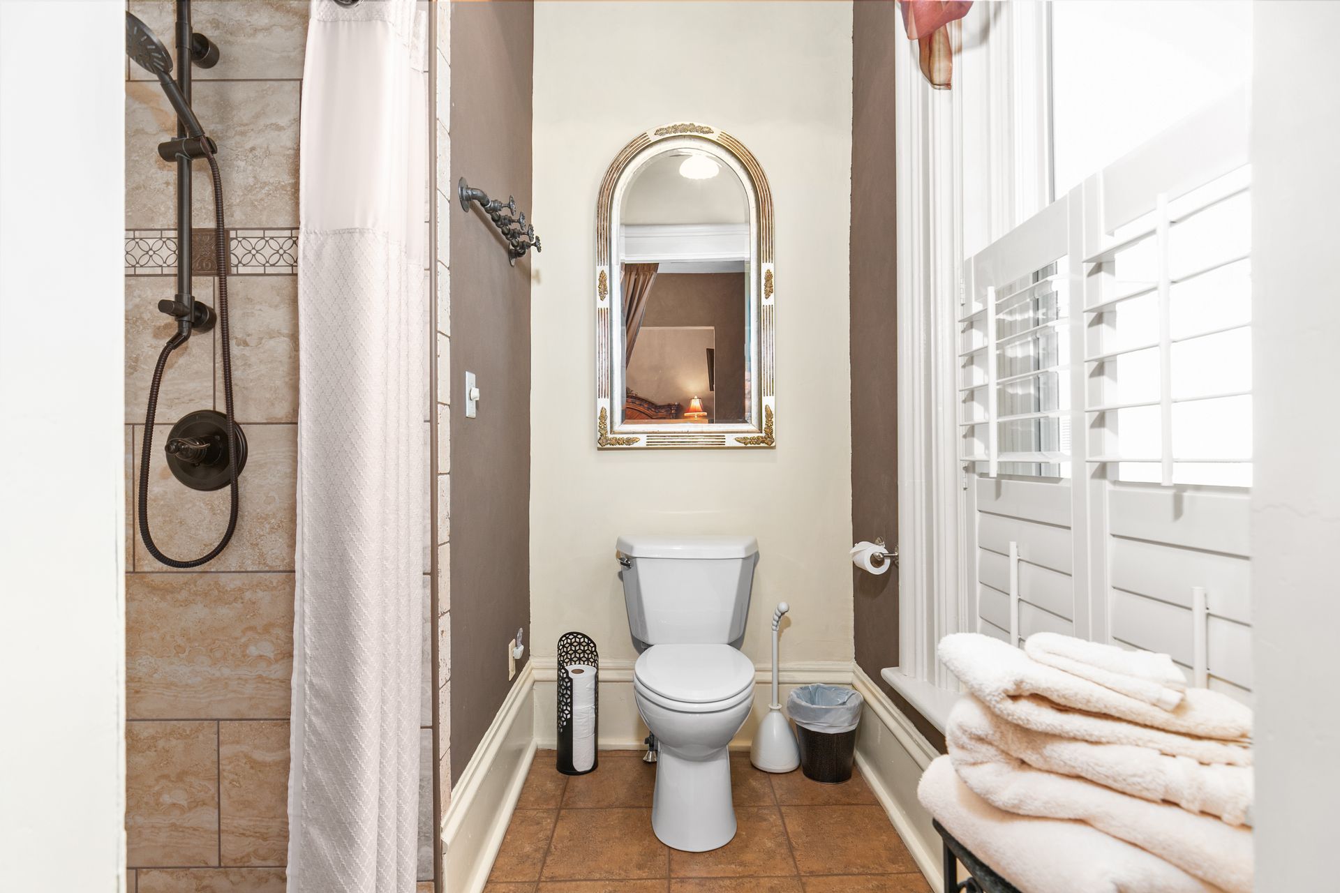 Bathroom with toilet, shower, mirror, and folded towels. Brown and white color scheme.