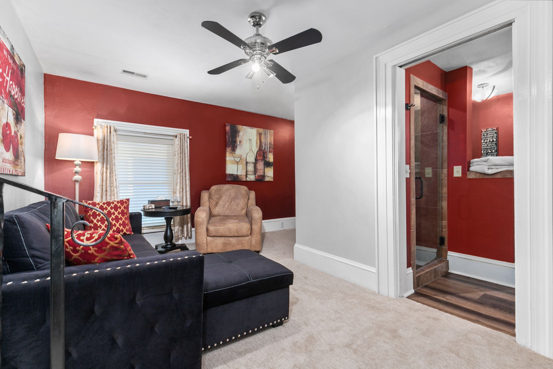 Cozy room with dark sofa, red walls, and a doorway to a bathroom with a dark wood-look door and red wall.